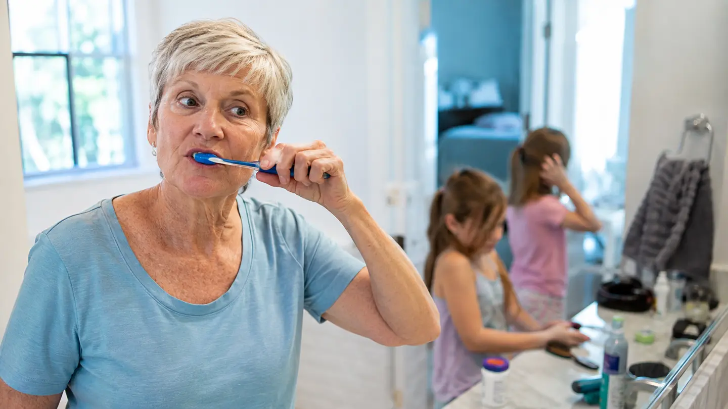 An older woman brushing her teeth during a busy family morning at home